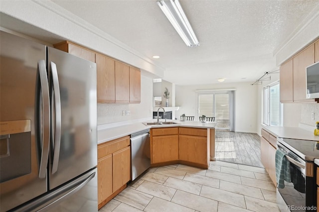 kitchen with a sink, a textured ceiling, stainless steel appliances, a peninsula, and light countertops