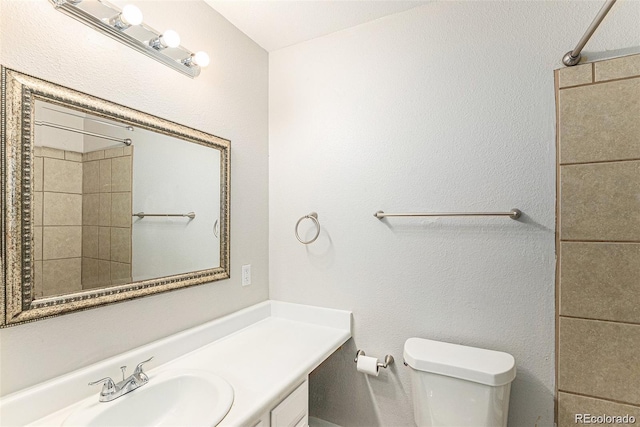 bathroom featuring tiled shower, vanity, and toilet