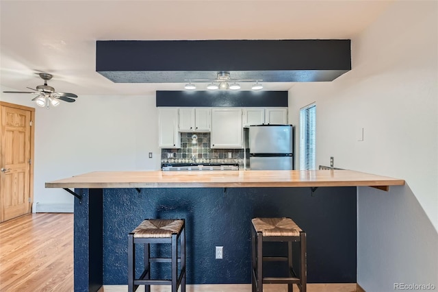695 Manhattan Dr Unit 109, Boulder, CO 80303 - kitchen with freestanding refrigerator, wood counters, decorative backsplash, a kitchen bar, and white cabinets