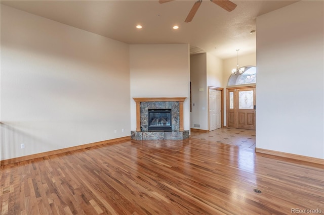 unfurnished living room featuring ceiling fan with notable chandelier, light hardwood / wood-style floors, and high vaulted ceiling