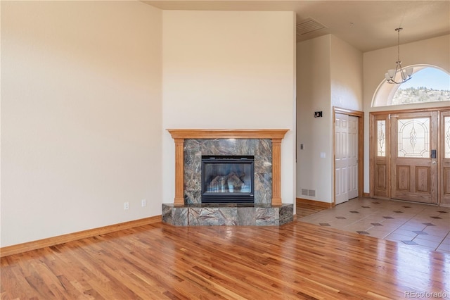 unfurnished living room featuring a high end fireplace, a notable chandelier, a towering ceiling, and light tile floors