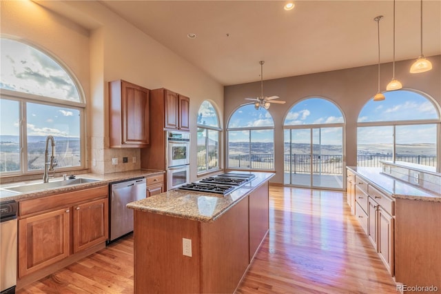 kitchen featuring appliances with stainless steel finishes, a center island, sink, backsplash, and light wood-type flooring