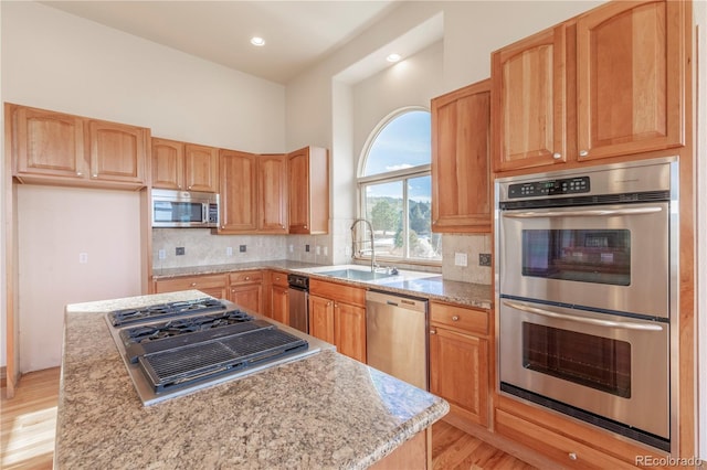 kitchen with appliances with stainless steel finishes, light hardwood / wood-style flooring, backsplash, and light stone counters