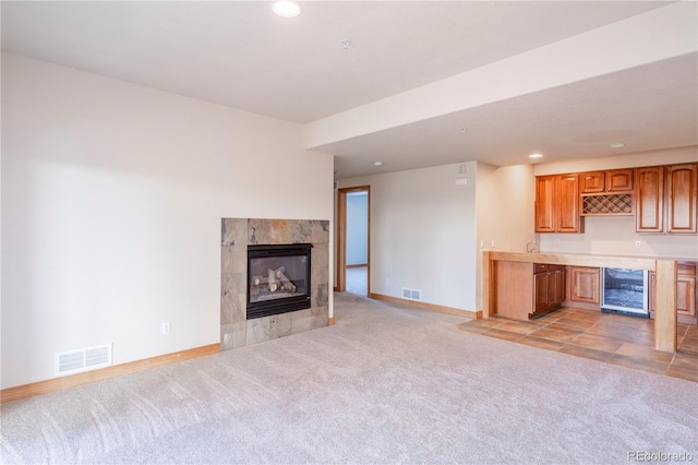 unfurnished living room featuring light carpet, beverage cooler, and a fireplace