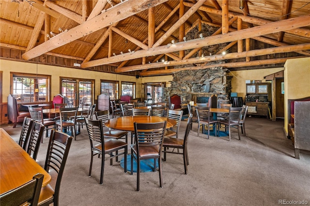 dining room with carpet floors, a stone fireplace, beamed ceiling, and high vaulted ceiling