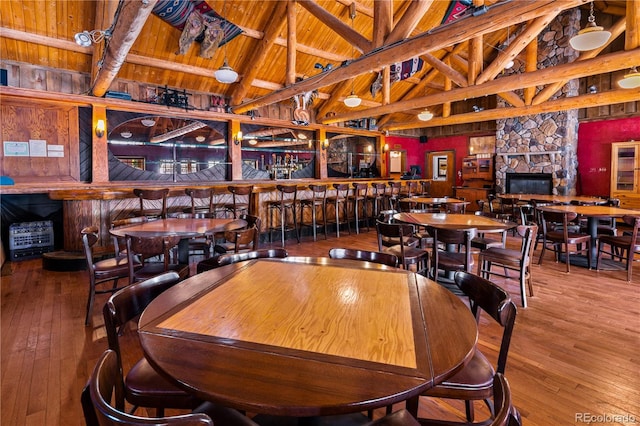 dining room with wood ceiling, high vaulted ceiling, a stone fireplace, beam ceiling, and hardwood / wood-style flooring