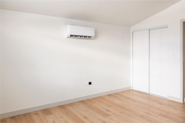 unfurnished bedroom featuring hardwood / wood-style floors, a closet, a wall mounted AC, and vaulted ceiling