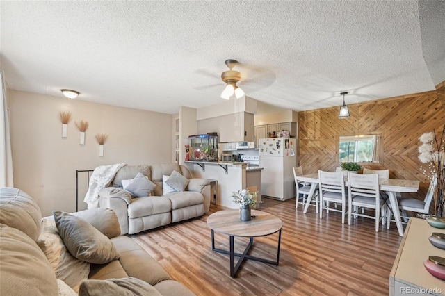 living room featuring wood walls, a ceiling fan, a textured ceiling, and wood finished floors