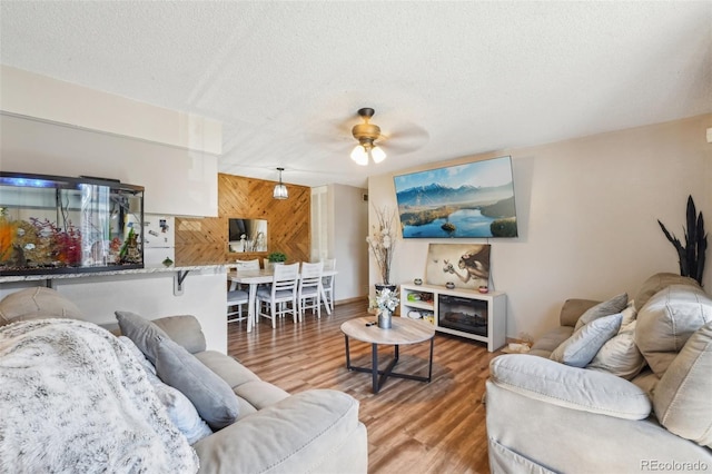 living room featuring a textured ceiling, a ceiling fan, wooden walls, and wood finished floors