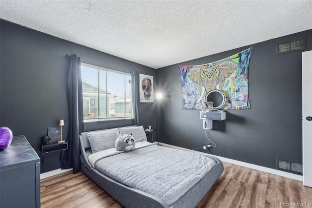 bedroom with wood finished floors, a textured ceiling, and baseboards