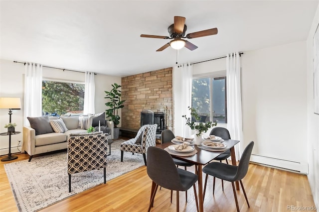 dining area with baseboard heating, a stone fireplace, ceiling fan, and light hardwood / wood-style floors