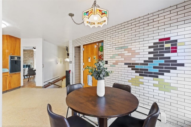 dining space featuring ceiling fan, a fireplace, brick wall, and a baseboard radiator