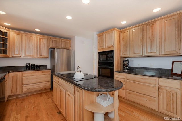 kitchen with dark stone counters, black appliances, a kitchen breakfast bar, light wood-type flooring, and light brown cabinetry