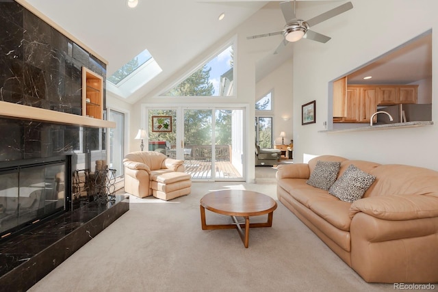 living room with carpet, a skylight, ceiling fan, high vaulted ceiling, and a premium fireplace