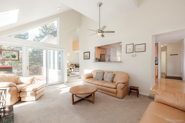 carpeted living room featuring a skylight, high vaulted ceiling, and ceiling fan