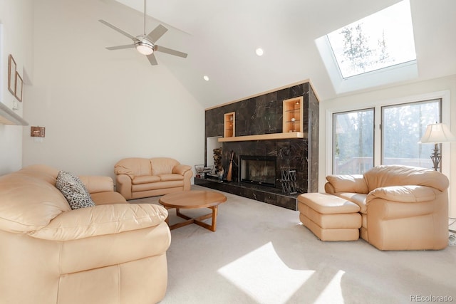 carpeted living room featuring a high end fireplace, a skylight, high vaulted ceiling, and ceiling fan