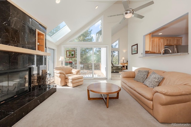 living room featuring ceiling fan, a skylight, high vaulted ceiling, a high end fireplace, and carpet floors