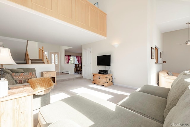 living room featuring light colored carpet, a ceiling fan, stairway, a baseboard heating unit, and baseboards