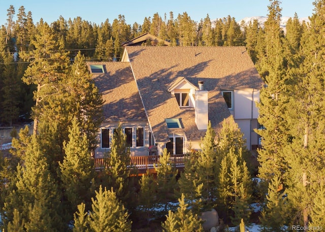 view of front of house with a view of trees and roof with shingles