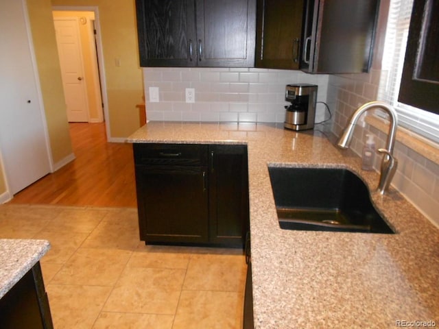 kitchen featuring decorative backsplash, light stone countertops, light wood-type flooring, dark brown cabinets, and sink