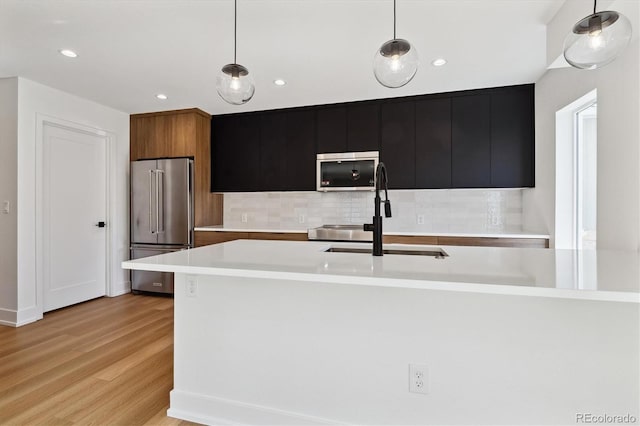 kitchen featuring a sink, light countertops, high end refrigerator, decorative light fixtures, and dark cabinets