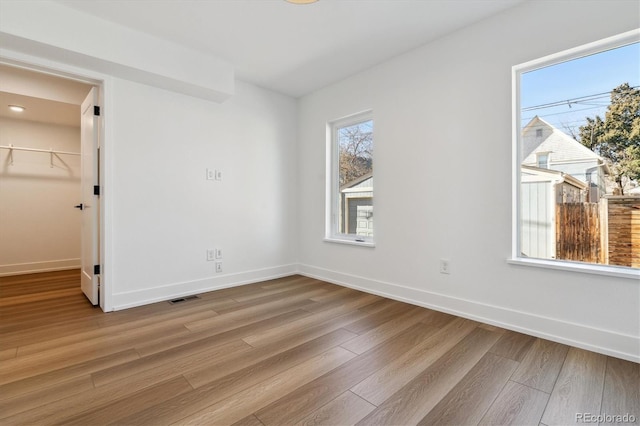 empty room with visible vents, light wood-style flooring, and baseboards