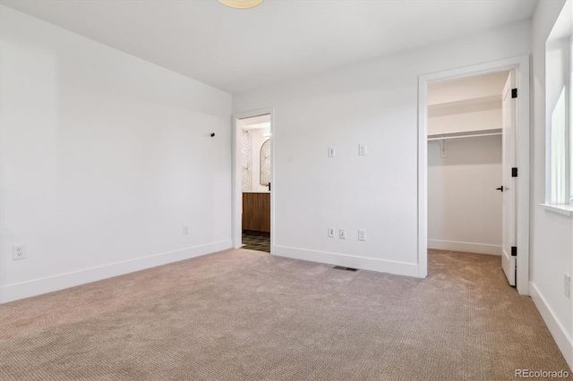 unfurnished bedroom featuring a walk in closet, carpet floors, and baseboards