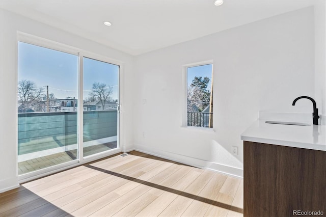 empty room with a sink, baseboards, light wood-style flooring, and recessed lighting