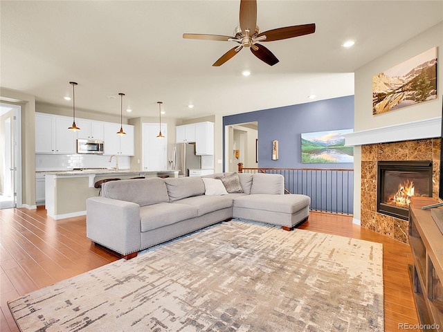 living area featuring light wood-type flooring, ceiling fan, a fireplace, and recessed lighting