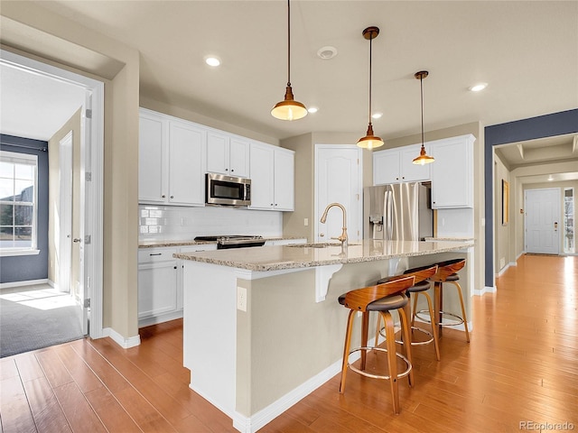 kitchen with a center island with sink, stainless steel appliances, backsplash, white cabinetry, and a sink