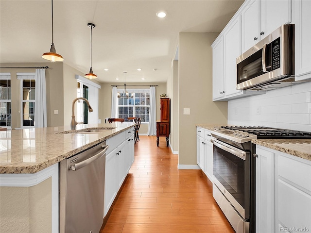 kitchen featuring a sink, stainless steel appliances, light wood-style floors, white cabinetry, and backsplash