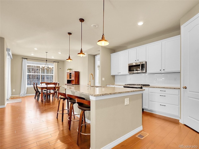 kitchen with a sink, visible vents, light wood-style floors, backsplash, and stainless steel microwave