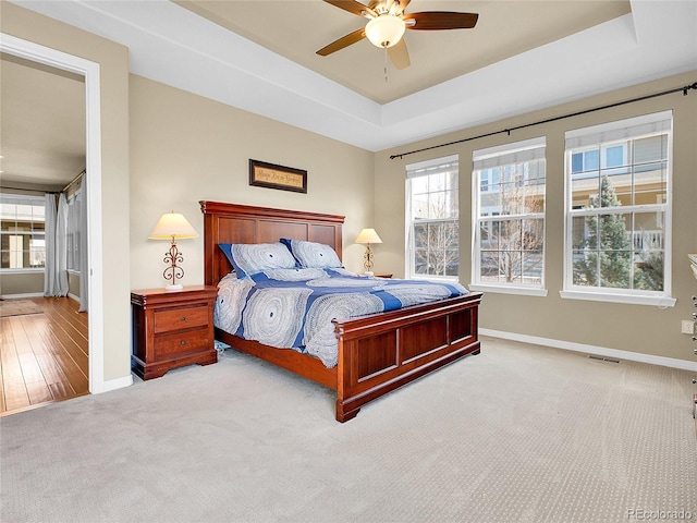 carpeted bedroom featuring a raised ceiling, multiple windows, and baseboards