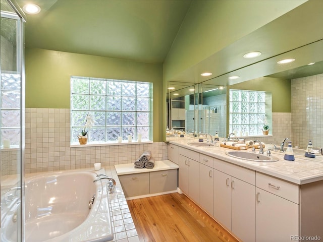 bathroom with vanity, lofted ceiling, hardwood / wood-style flooring, tile walls, and tiled tub