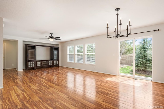 interior space with wood finished floors, ceiling fan with notable chandelier, baseboards, and a healthy amount of sunlight