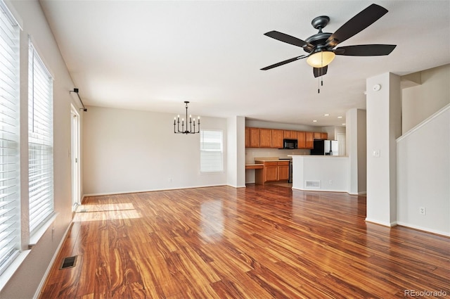 unfurnished living room featuring wood finished floors, ceiling fan with notable chandelier, and visible vents