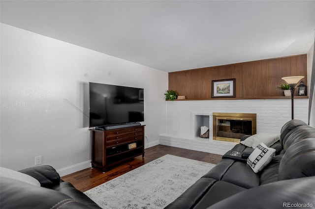 living room with a brick fireplace and dark wood-type flooring