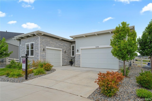 view of front of property with a garage, stone siding, driveway, and fence