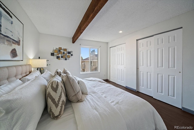 bedroom featuring baseboards, dark wood-style floors, beamed ceiling, a textured ceiling, and multiple closets