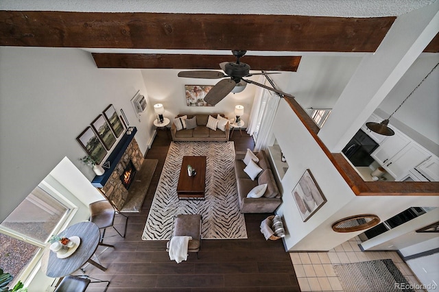 living room featuring ceiling fan, a fireplace, wood finished floors, a healthy amount of sunlight, and beam ceiling