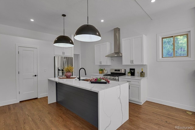 kitchen with a kitchen island with sink, white cabinetry, wall chimney range hood, stainless steel appliances, and light stone countertops