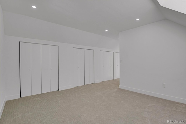 unfurnished bedroom with lofted ceiling, light colored carpet, and multiple closets