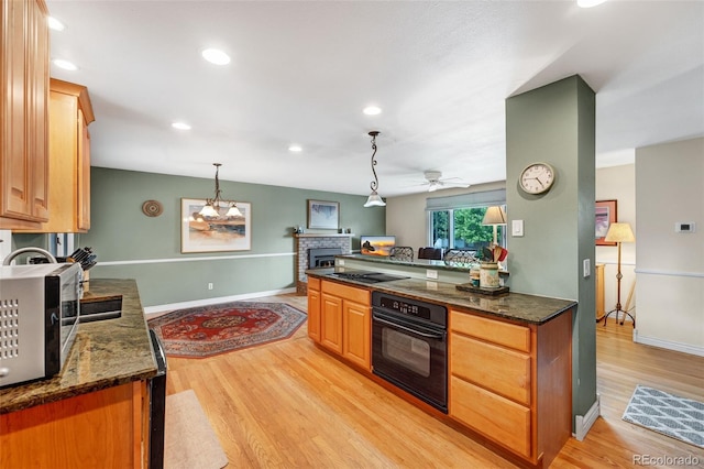 1161 S Johnson Way, Lakewood, CO 80232 - kitchen featuring black appliances, a fireplace, light wood-type flooring, a ceiling fan, and dark stone countertops