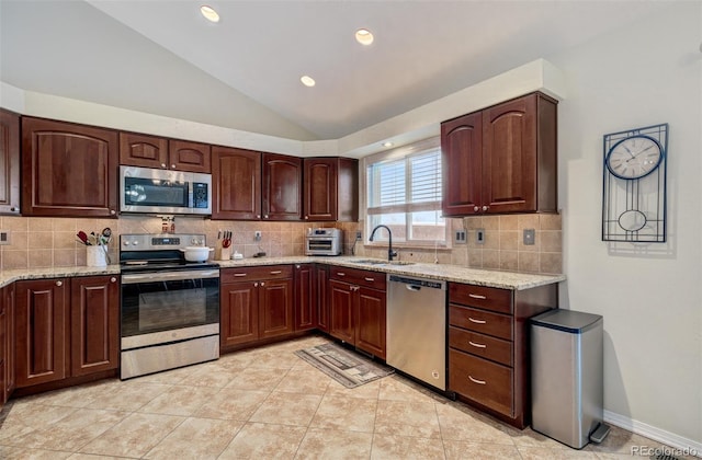 kitchen with light stone countertops, appliances with stainless steel finishes, vaulted ceiling, and sink