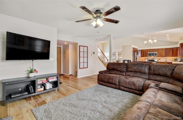 living room with ceiling fan with notable chandelier, light hardwood / wood-style flooring, and vaulted ceiling