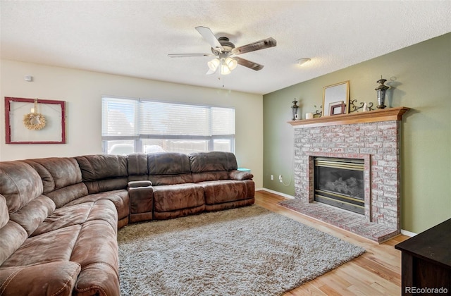 living room with a textured ceiling, ceiling fan, a fireplace, and light hardwood / wood-style flooring