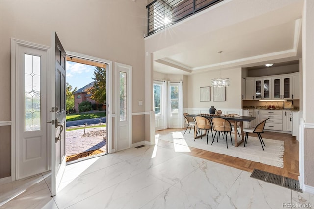 entryway with light wood-type flooring, a chandelier, a wealth of natural light, and a tray ceiling