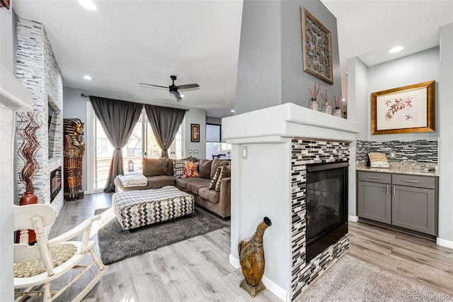 living room with a tiled fireplace, light hardwood / wood-style floors, and ceiling fan