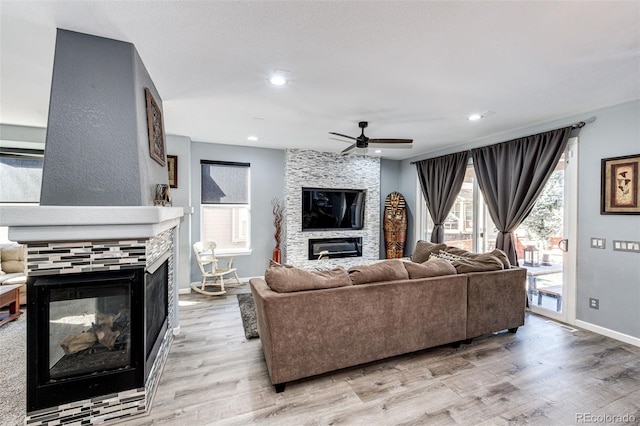 living room featuring a fireplace, ceiling fan, and light wood-type flooring