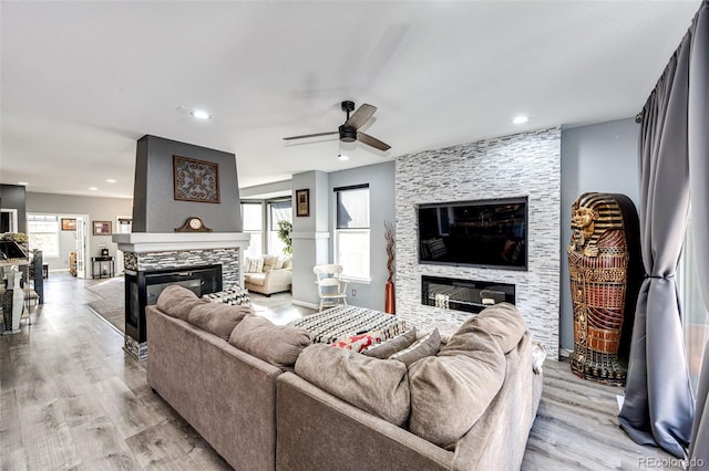 living room with ceiling fan, a stone fireplace, and a wealth of natural light